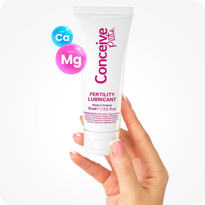 For Conceive Plus Fertility Lubricant Combo 75ml + 8 applicators (DE), image showing a hand holding 75ml fertility lubricant tube upright, with highlighted calcium (Ca) and magnesium (Mg) ions floating beside it, visually emphasizing pH-balancing ingredients that support fertility in this German-labeled product.