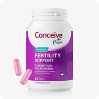 For Conceive Plus Fertility Supplement & Lubricant For Women (DE), bottle of women's fertility support multivitamins, featuring a white and purple label, 60 vegan capsules, and two pink capsules placed beside container on a white background.