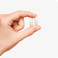 Hand holding two beige Conceive Plus Birth Control Detox vegan capsules against a white background, showing size and appearance of supplement for daily use after stopping birth control.
