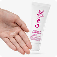 Conceive Plus Fertility Lubricant 75ml tube held beside an open female hand with a visible amount of clear lubricant gel on the palm. Set against a white background to highlight product texture and application.