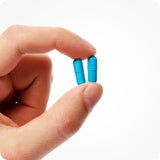 For Conceive Plus Men's Fertility Support + Lubricant (DE), close-up of two bright blue men fertility support capsules held between fingers, showing actual supplement size and texture, designed to support male reproductive health with essential vitamins and minerals.